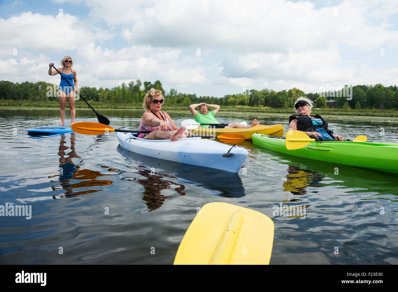 Family of senior woman with three adult children are paddling kayaks and paddleboards across a lake in northern Minnesota Stock Photo