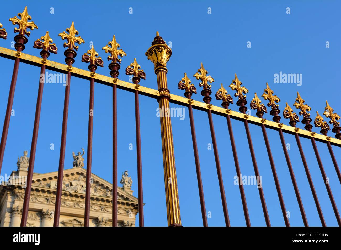 Red and gold iron fence against blue sky in front of a classical building Stock Photo