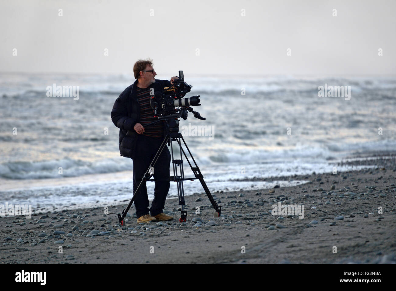 A documentary maker prepares for a shot at a New Zealand beach on sunset Stock Photo