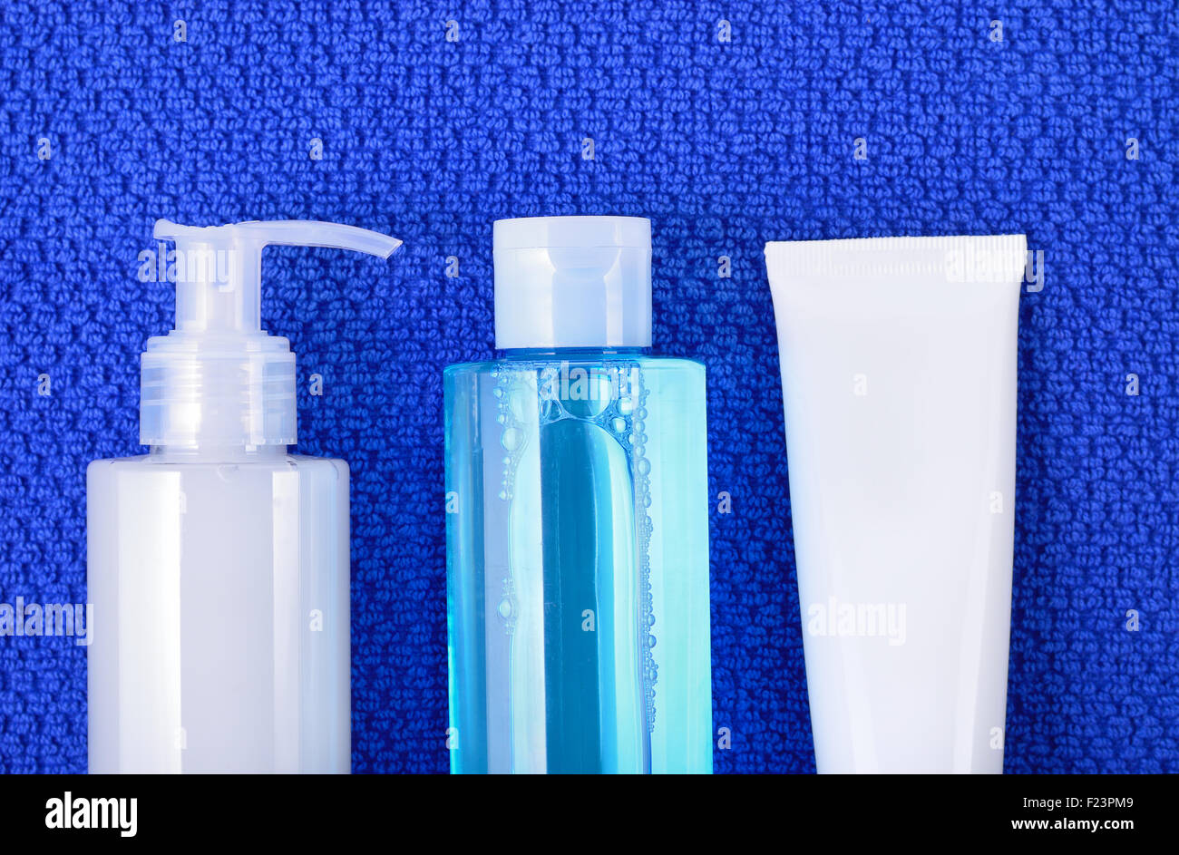 Daily basic care cosmetics - face wash cleansing gel, smoothing toner and cream on navy blue towel. Top view. Stock Photo
