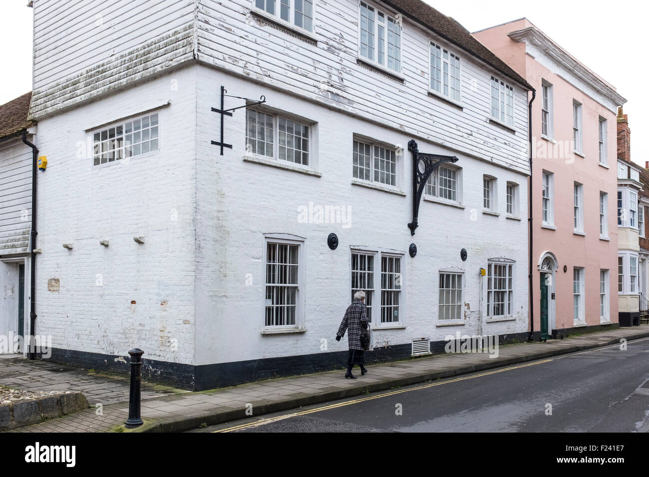 Older woman walks past a white painted old house with upper story clap ...