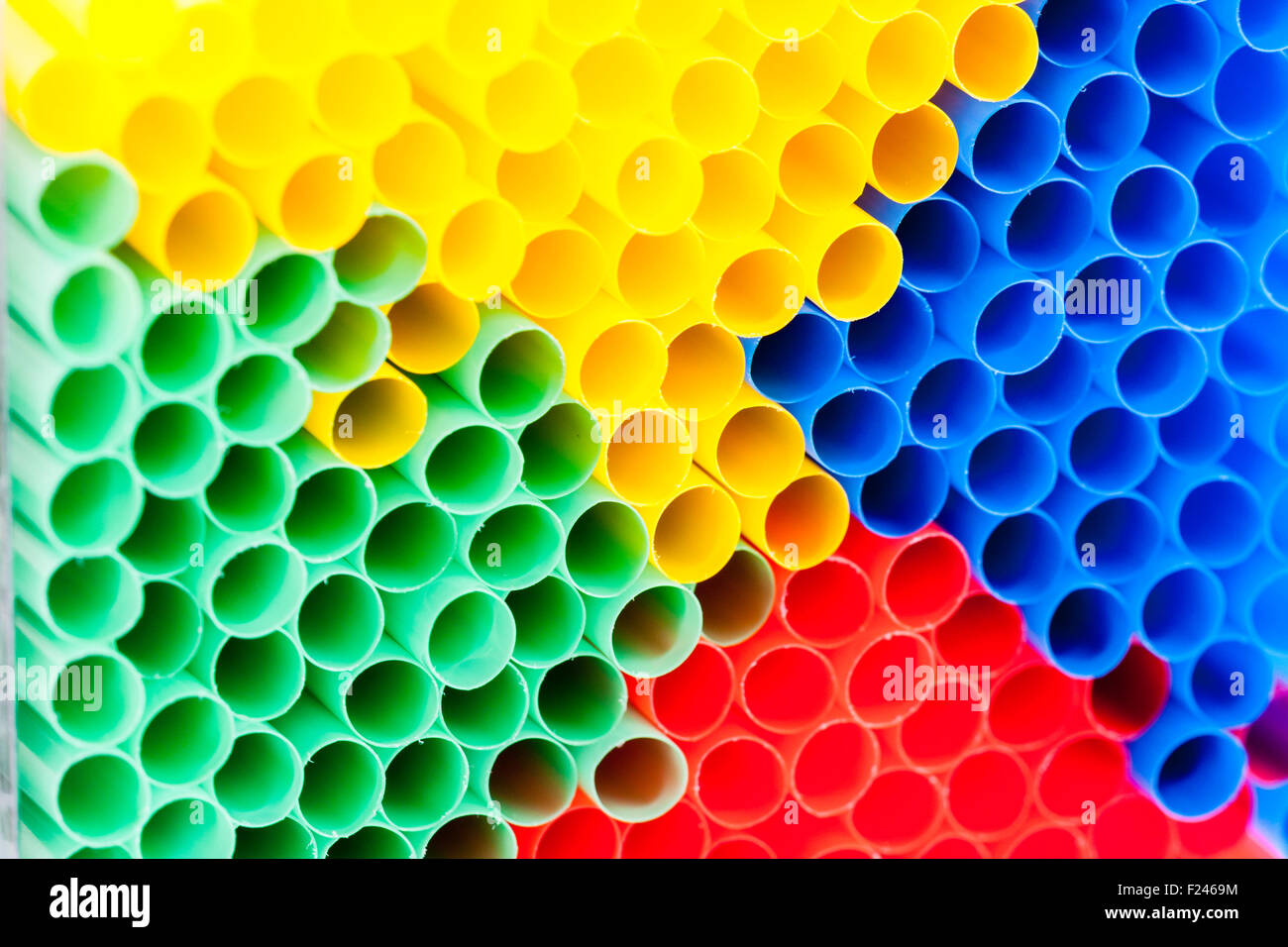 Macro close up of a frame to frame bundle of green, yellow, blue and red plastic drinking straws seen head on, forming abstract pattern. Stock Photo