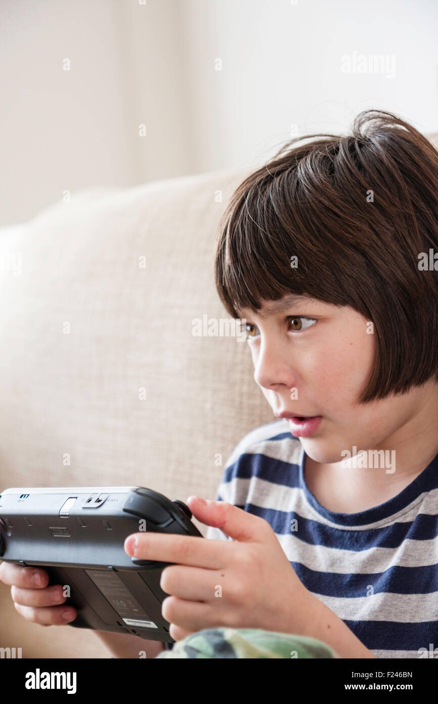 Male Caucasian child, boy, 10-12 year old, sitting holding a  Nintendo wii game console in both hands concentrating, head and shoulder side view. Stock Photo