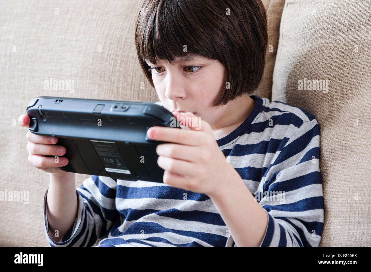 Male Caucasian child, boy, 10-12 year old, sitting holding a  Nintendo wii game console in both hands concentrating, head and shoulder side view. Stock Photo