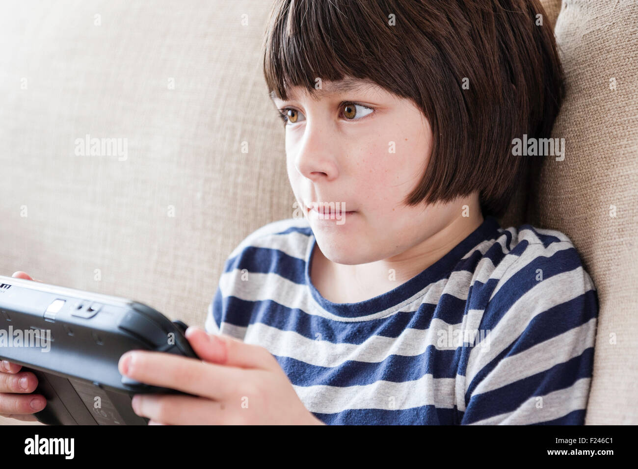 Male Caucasian child, boy, 10-12 year old, sitting holding a  Nintendo wii game console in both hands concentrating, head and shoulder side view. Stock Photo