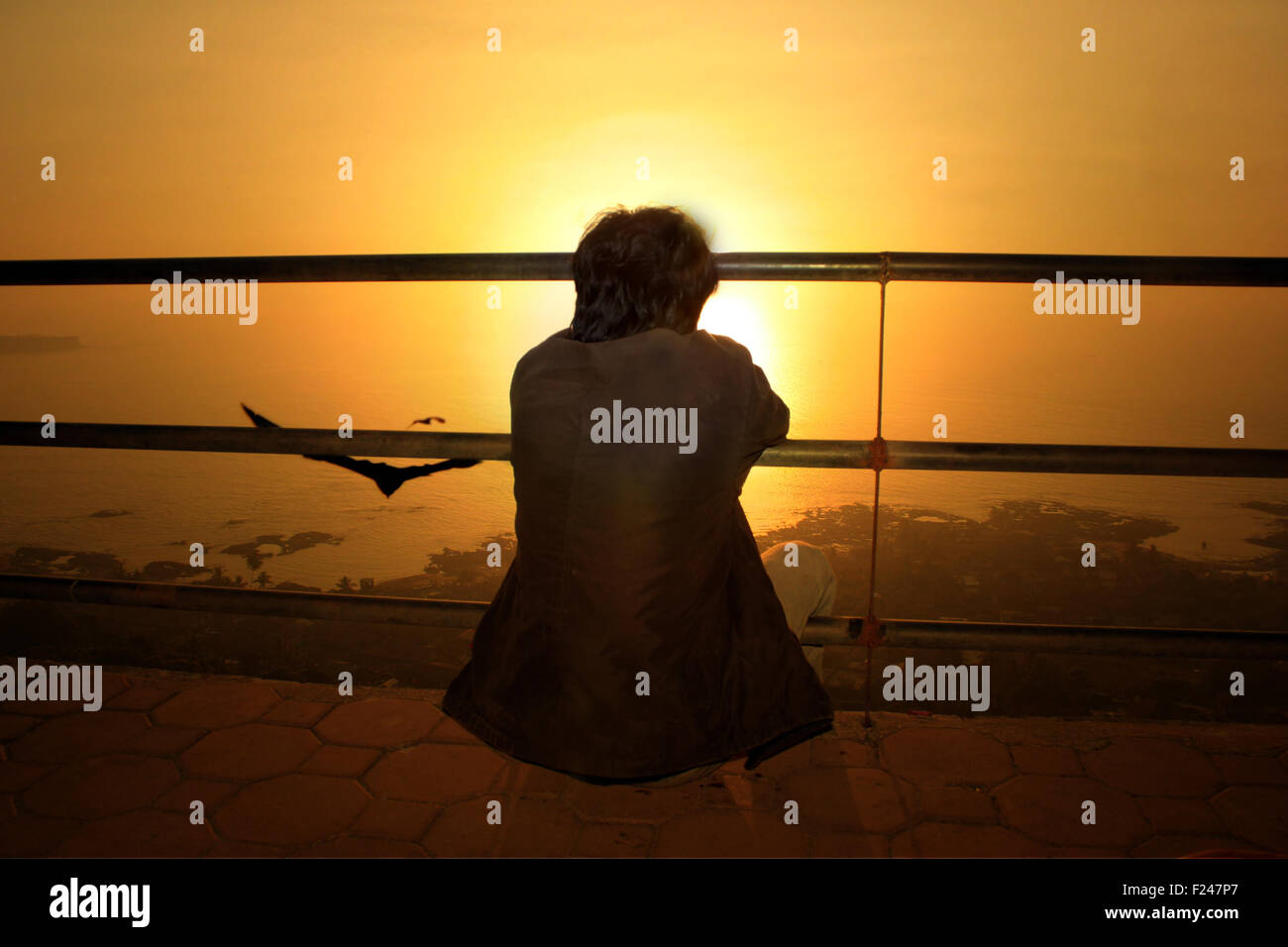 A metaphorical image of a contemplating lonely man looking at the setting sun. Stock Photo