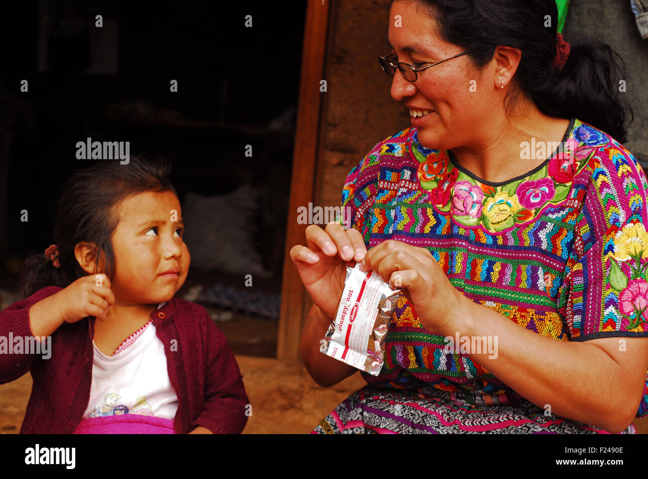 Guatemala, San Bartolo, nurse (Faustina vicenta vasquez Vasquez 34 years) opening plumpy nut pack for little indigenous girl (Orbelina Nataly Sontay Ramirez 3) Stock Photo