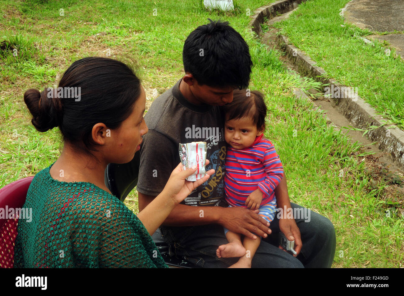 Guatemala, San Cristobal, child sitting on knee of father and eating plumpy nut (Cristobal Pop Calel 23, Erma Cecilia Tul Cal 17, Evelyn Glensi Pop Tul 1 year 1 mes) Stock Photo