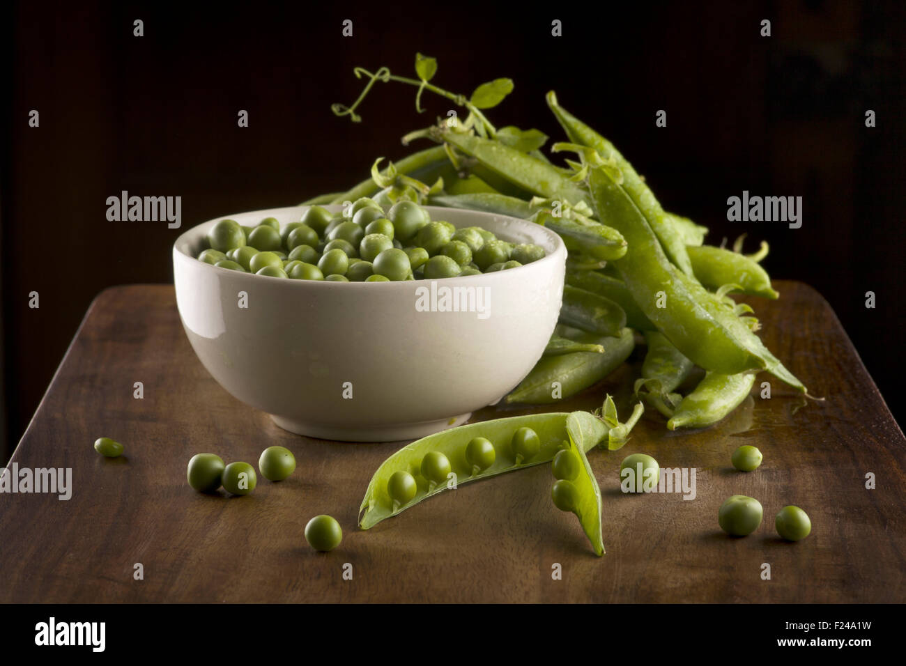 Fresh green peas with pods in the bowl on the wooden table Stock Photo