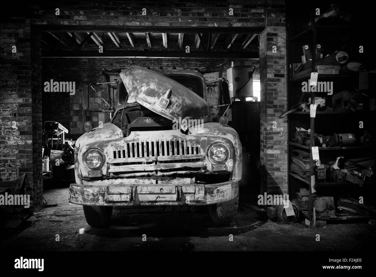 A black and white image of an old truck with a lot of character is parked with its hood up in a brick garage. Stock Photo