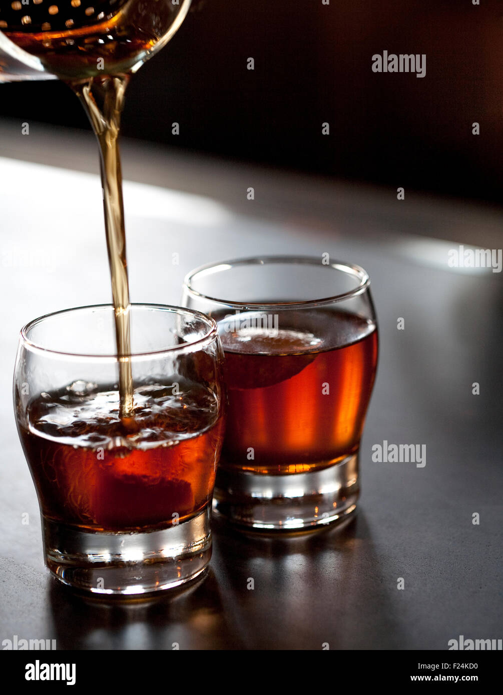 two backlit negroni cocktails in short glasses, the front one being poured from a cocktail shaker above Stock Photo