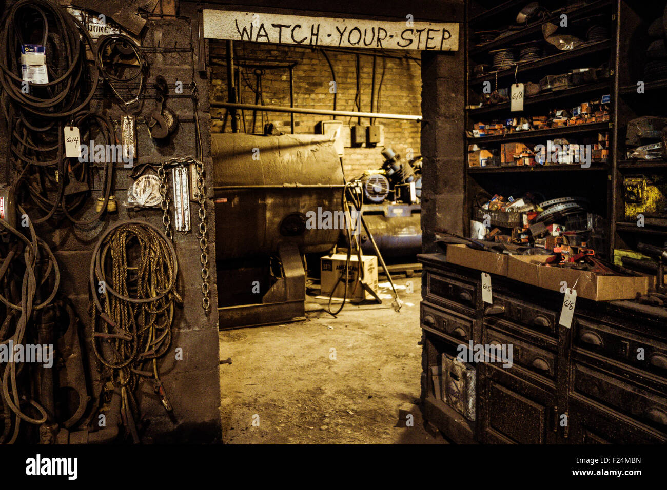 Equipment and parts are everywhere around a doorway into a boiler room, above which a sign warns 'Watch Your Step' Stock Photo