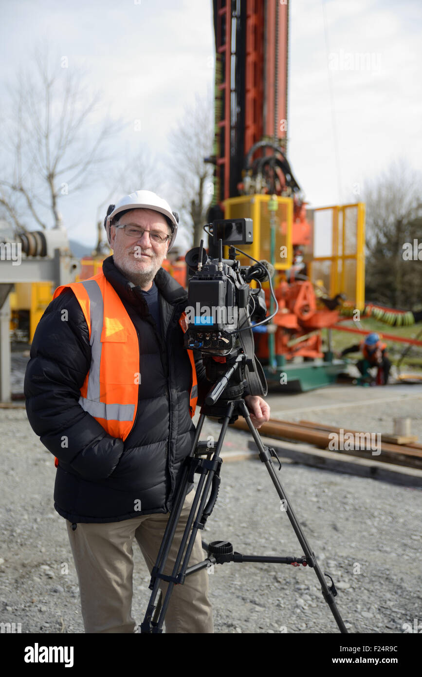 A documentary filmmaker poses with his camera on location at a drilling site Stock Photo