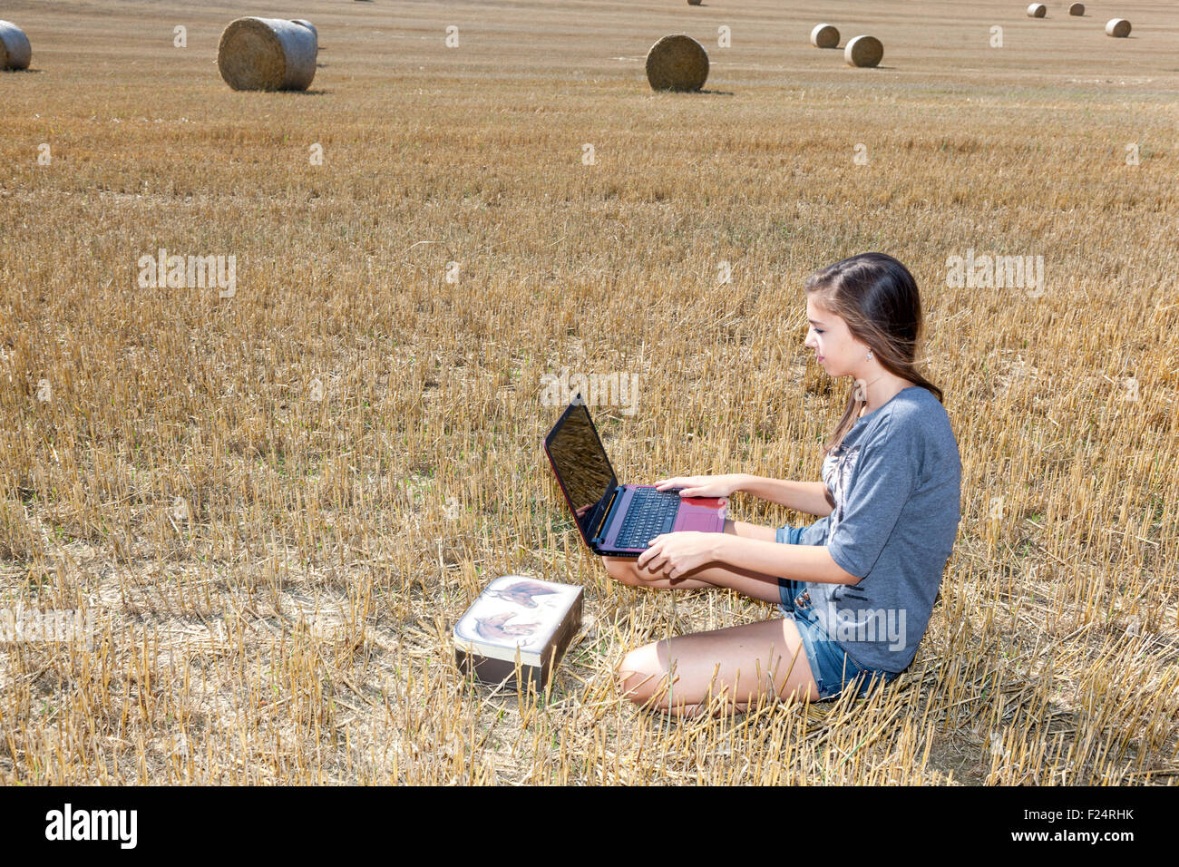 Young teenage beautiful girl with a laptop on stubble field Stock Photo
