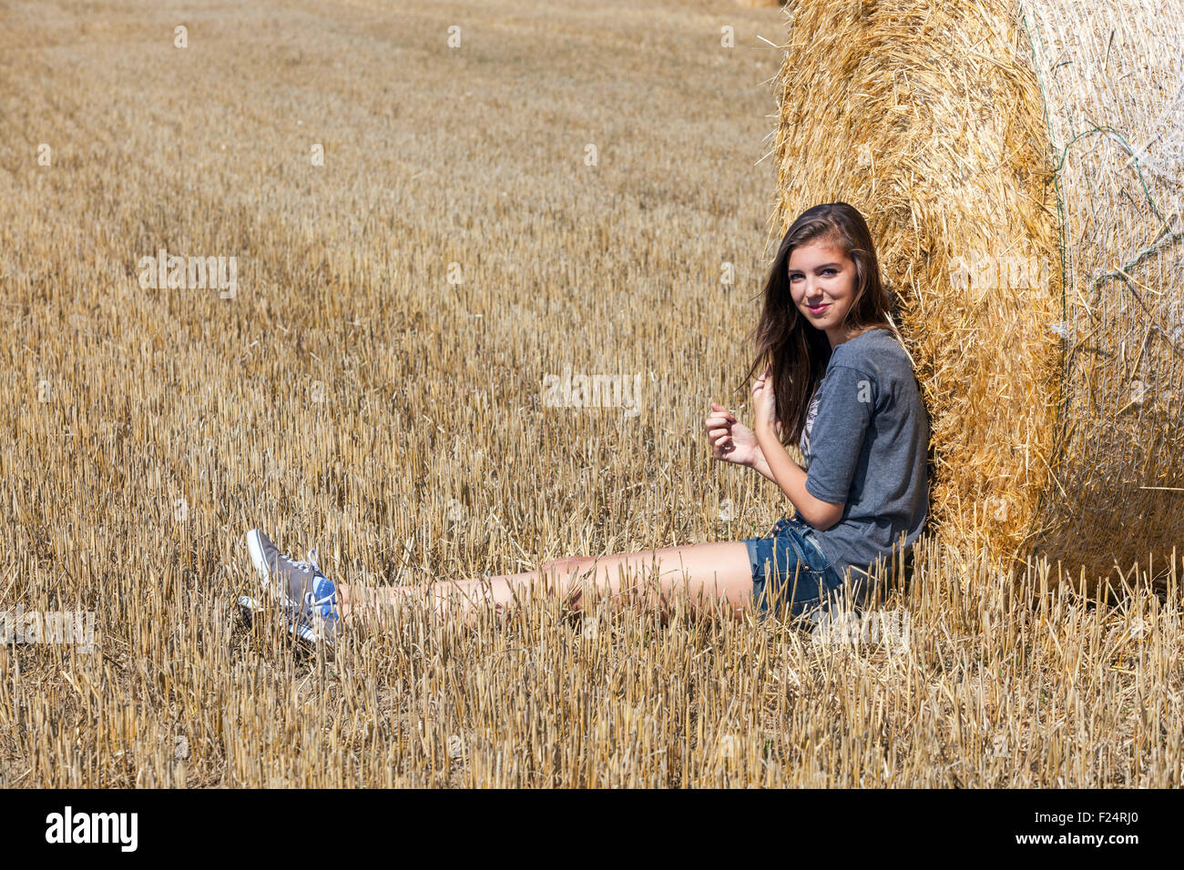 Young beautiful girl on straw bale, long legs Stock Photo