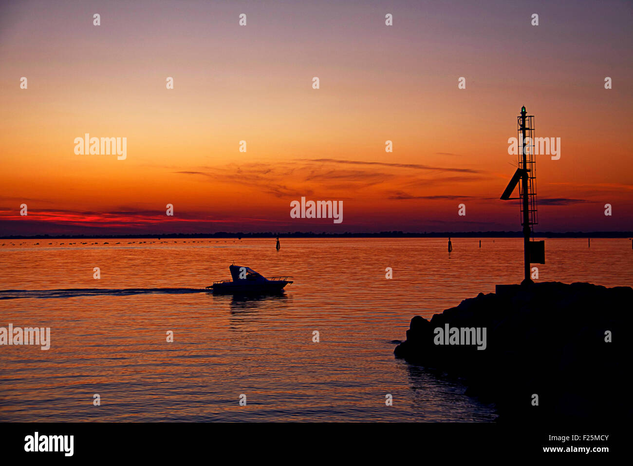 red sunset on sea harbor with silhouette of motor boat and green entrance light Stock Photo