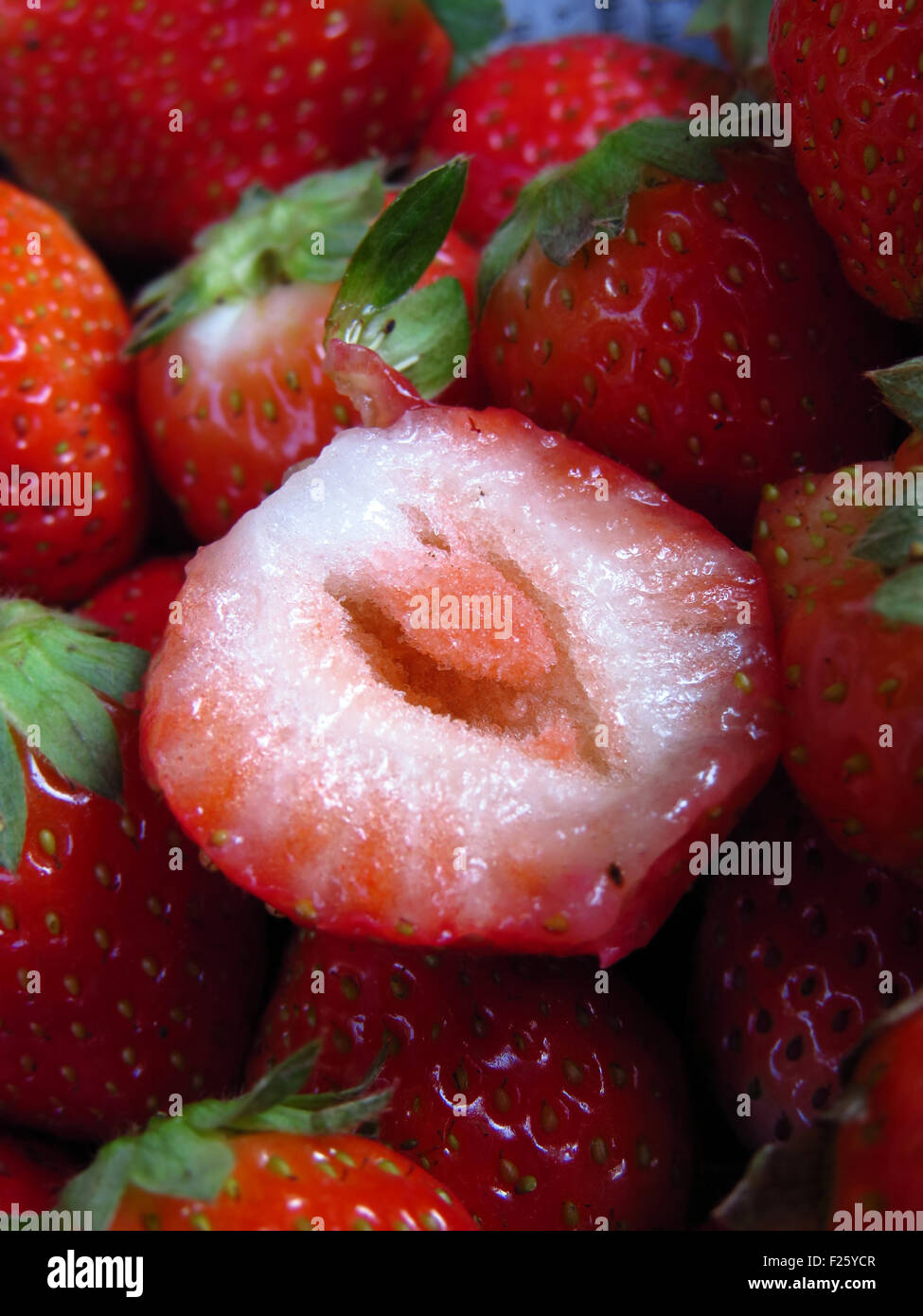 A cut delicious strawberry on a stack of fresh ripe strawberries. Stock Photo