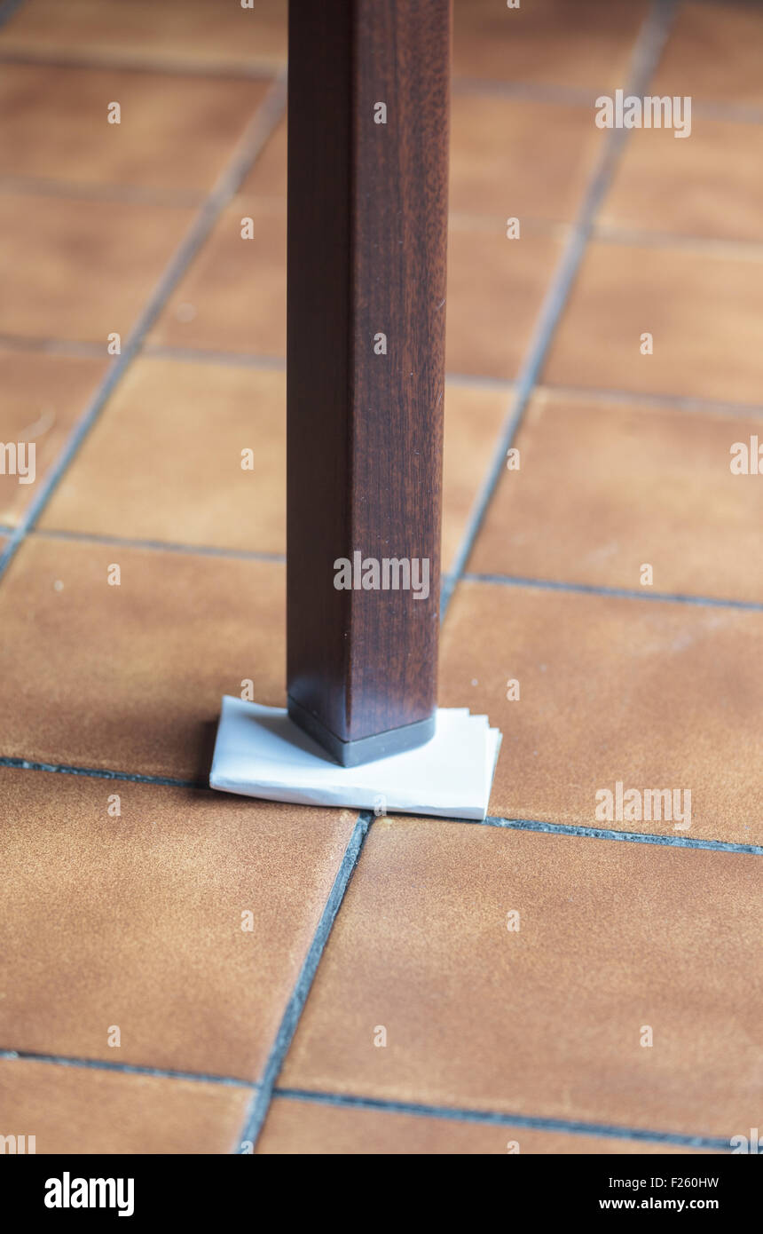 Leg of a wobbly table supported by folded paper Stock Photo