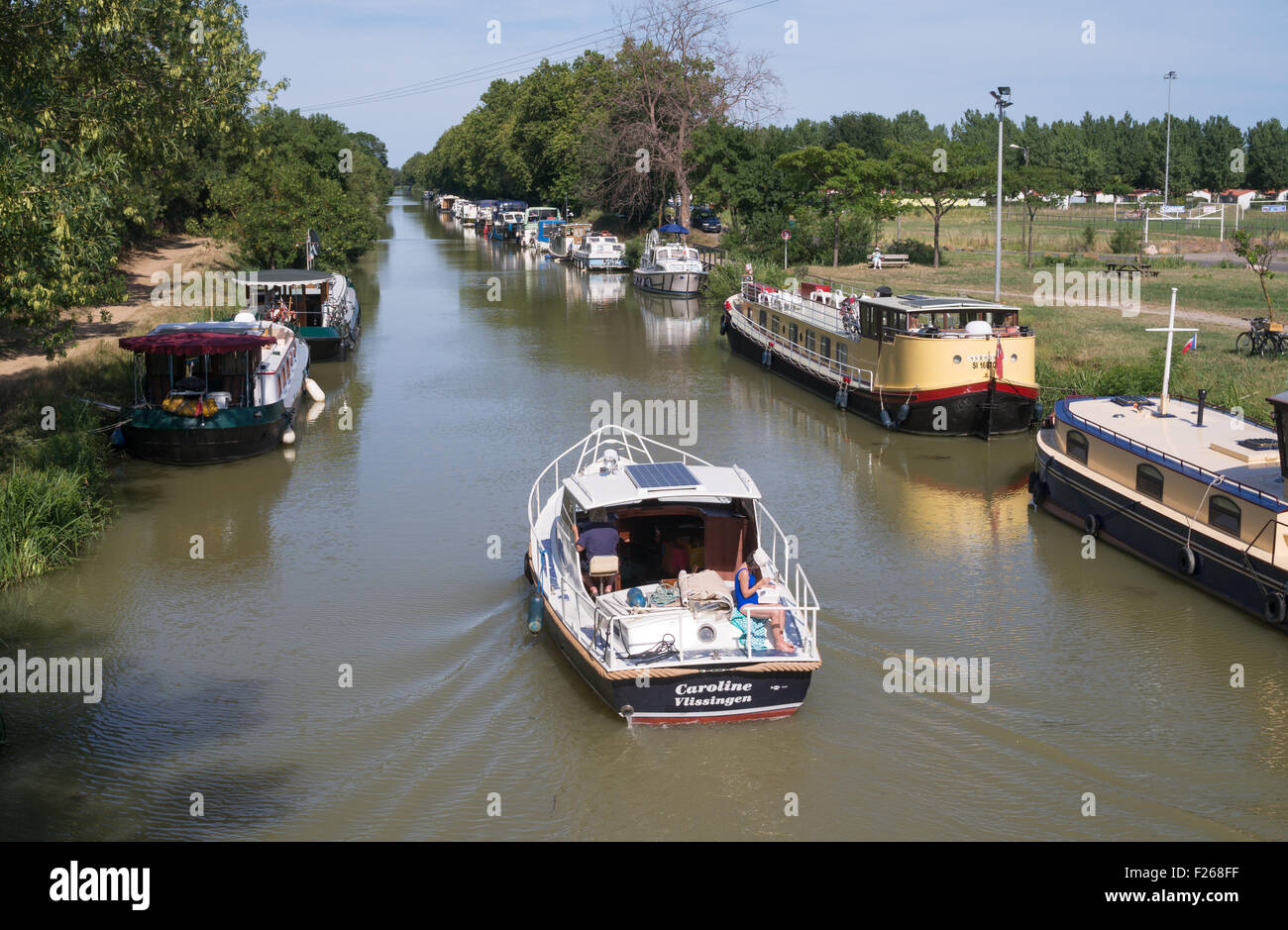 A boat on the Canal du Midi passing moored vessels at Vias, Hérault, Languedoc-Roussillon, France Stock Photo