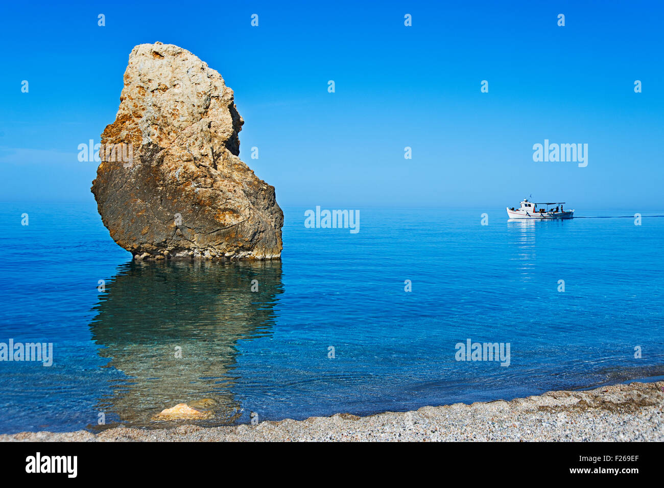 Fishing boat passing a rock at the Aegean coast of Pelion Peninsula, Thessaly, Greece Stock Photo