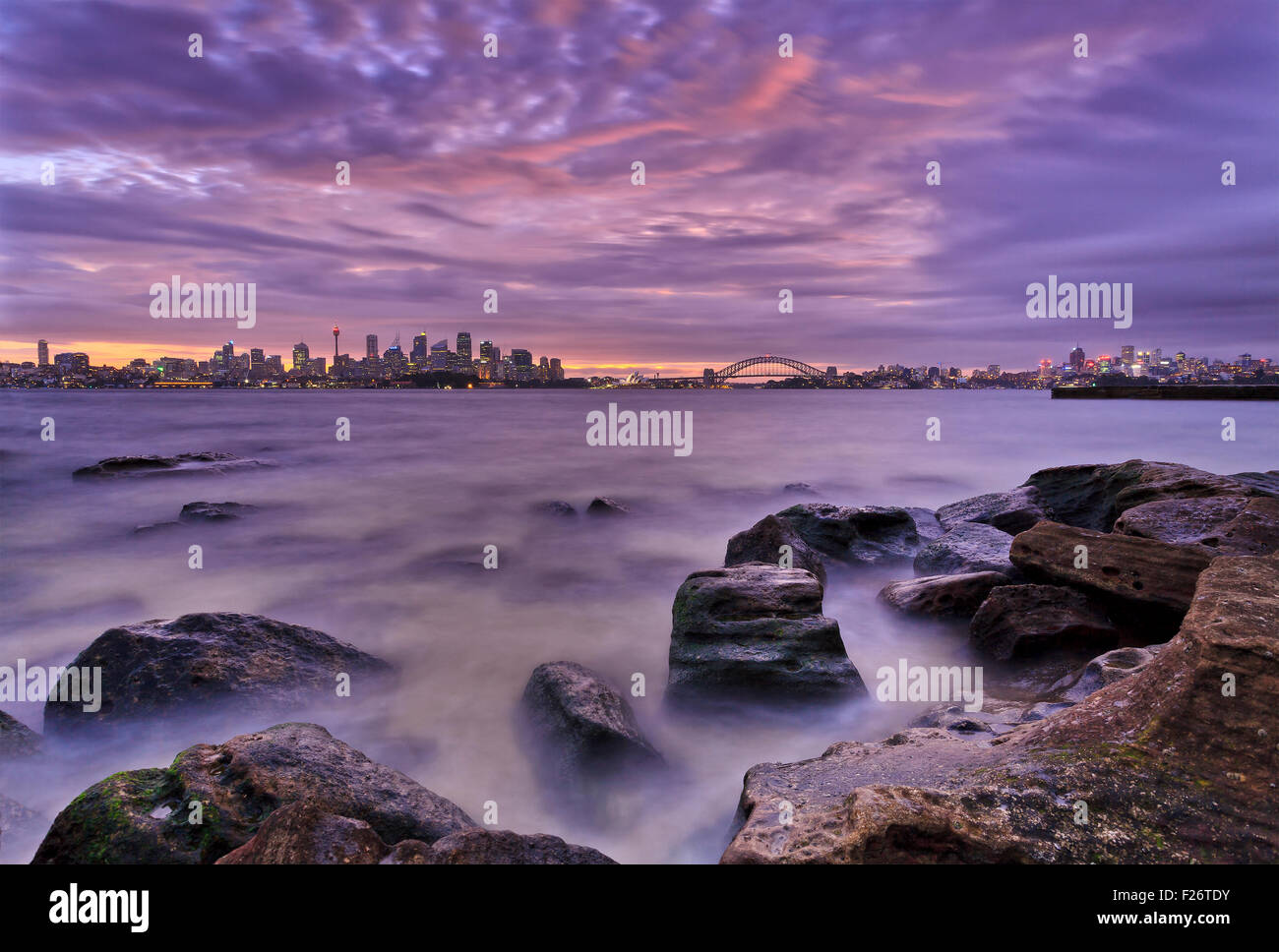 Natural seascape with distant Sydney city CBD landmarks across harbour at low tide during cloudy sunset Stock Photo