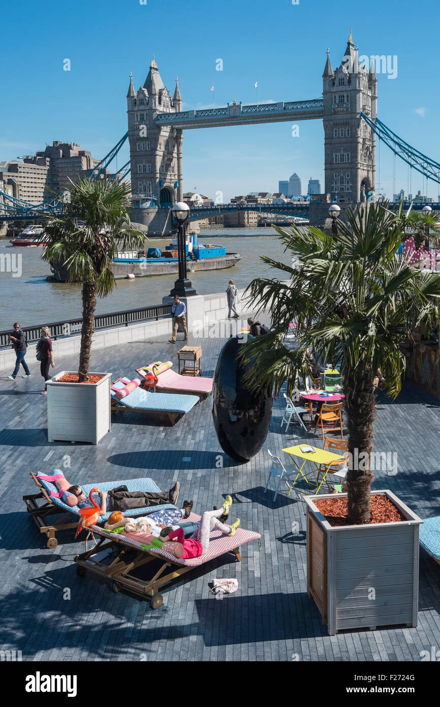 People relaxing in summer sunshine at London Riviera pop up restaurant, with iconic Tower Bridge in the background, England UK Stock Photo