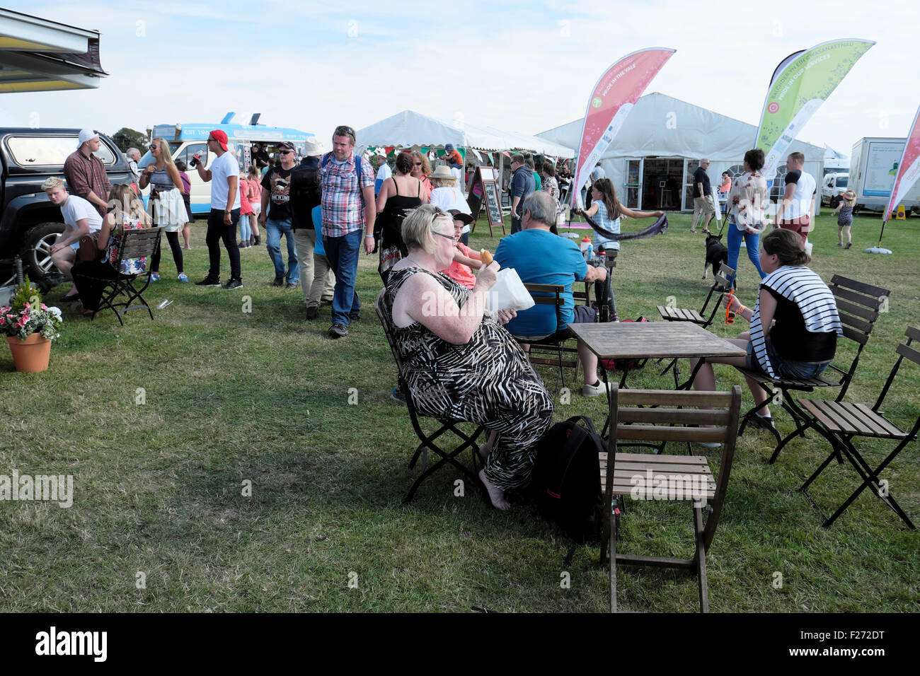 Older woman sitting outside at picnic table with crowd eating donuts doughnut at agricultural show in UK  KATHY DEWITT Stock Photo