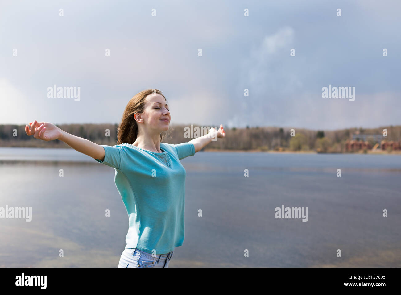 Freckled happy girl with outstretched arms smiling to sun and closing her eyes Stock Photo