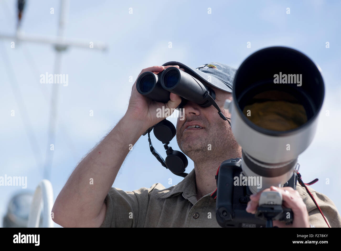 Wildlife photographer using binoculars to look for animals on a boat in Southeastern Alaska. Stock Photo