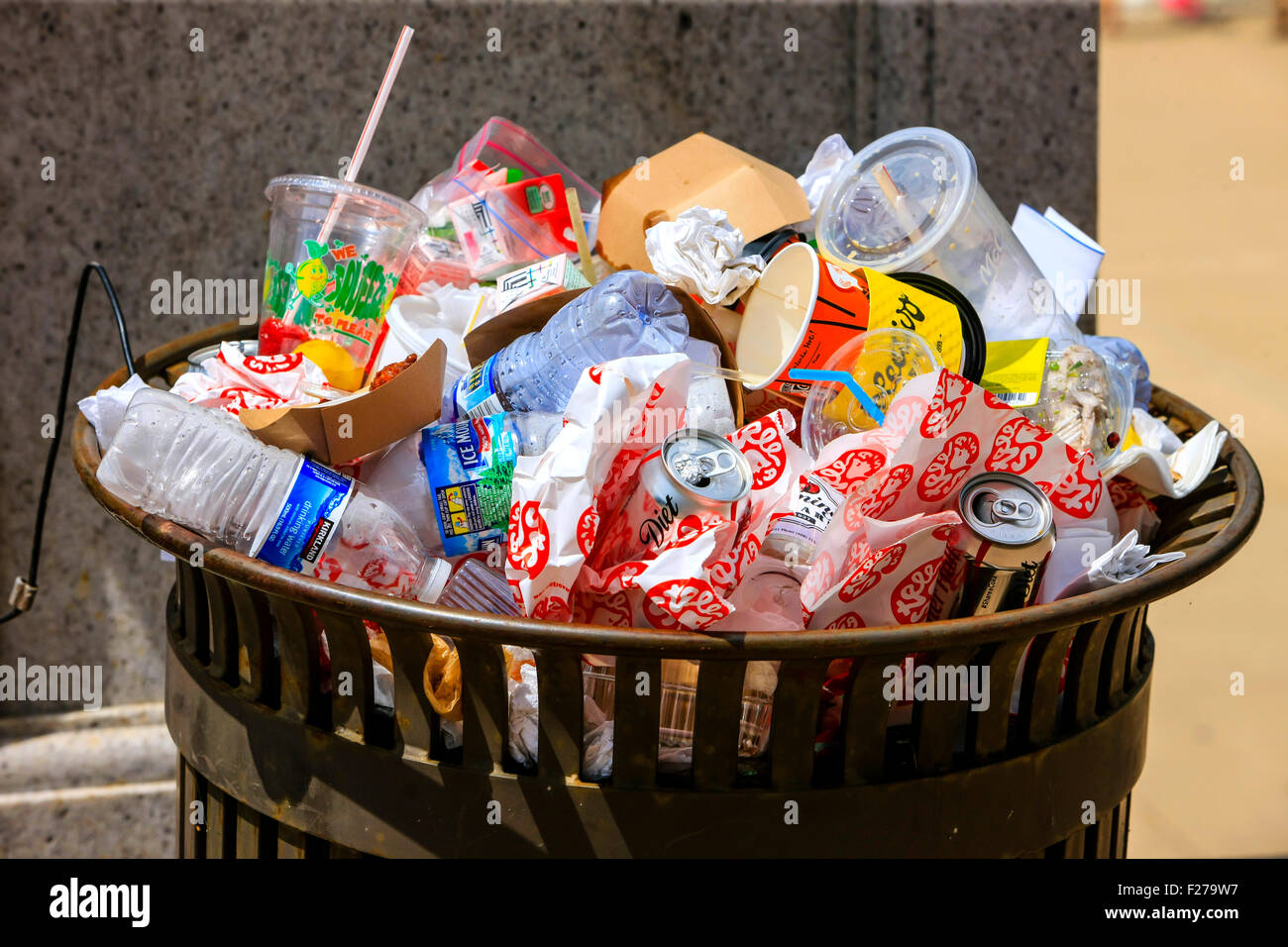 A trash can overflowing with empty drinks containers and food wrappers