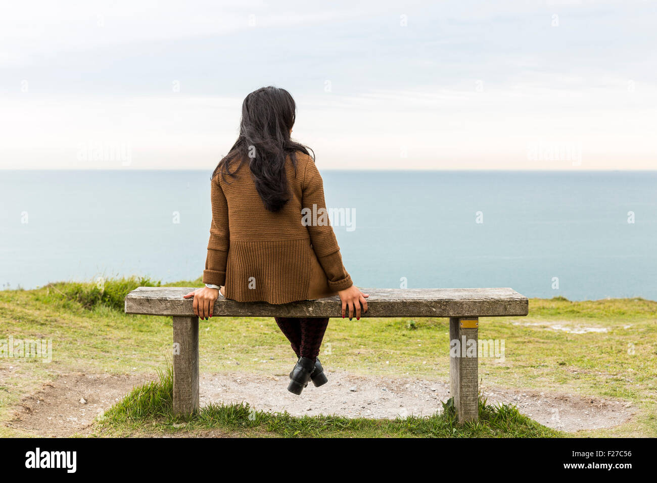 Back of a young woman sitting on a bench and looking at the sea. The ...