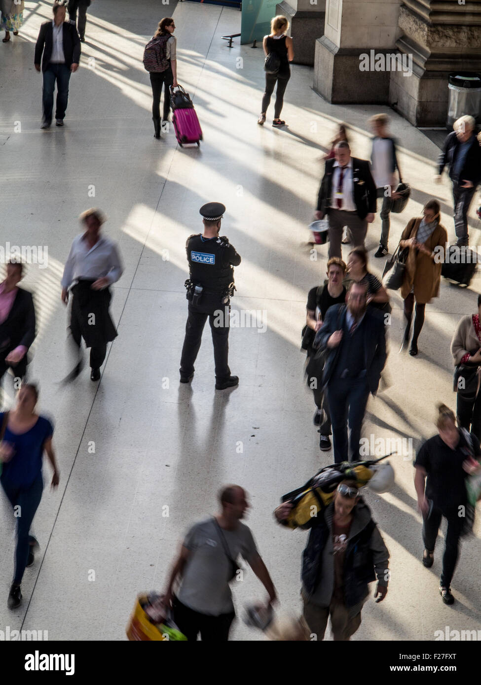 A lone policeman stands guard in a rush hour station with commuters rushing by him Stock Photo