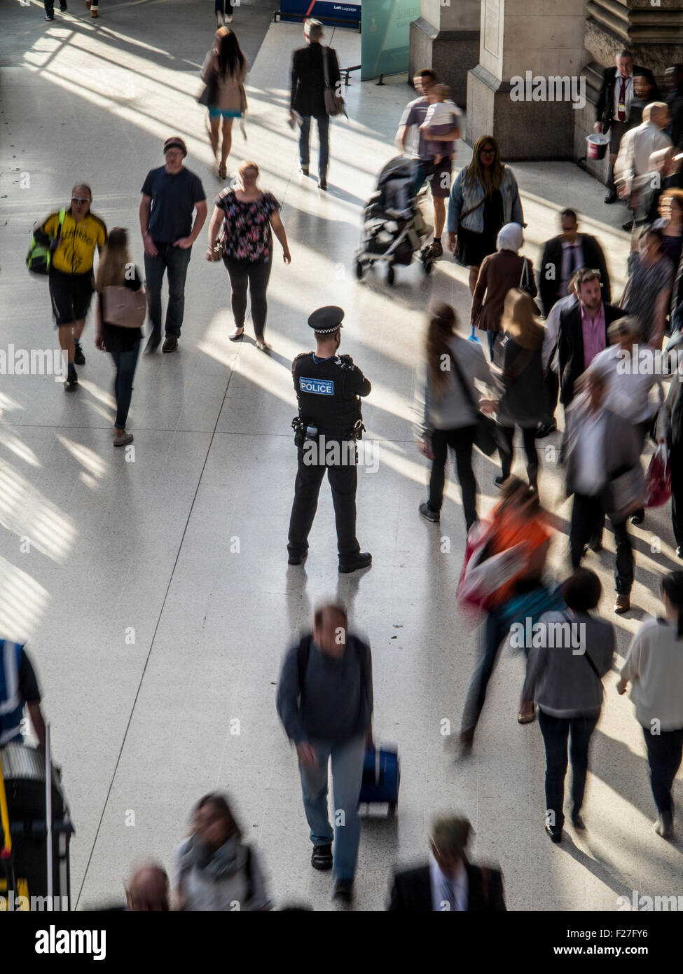 A lone policeman stands guard in a rush hour station with commuters rushing by him Stock Photo