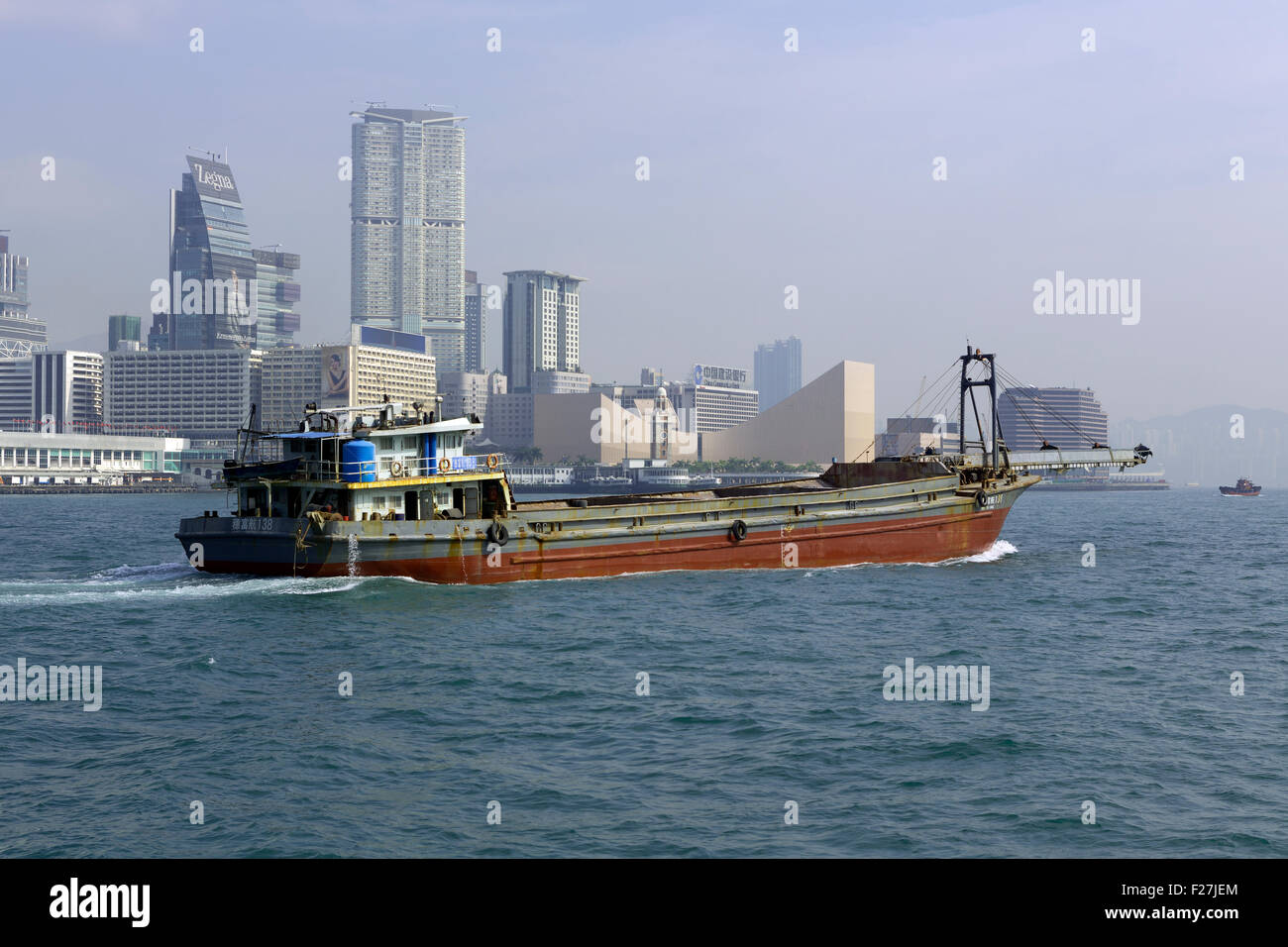 Small freighter moving through Victoria harbor Hong Kong. Tall buildings of Kow Loon in the background Stock Photo