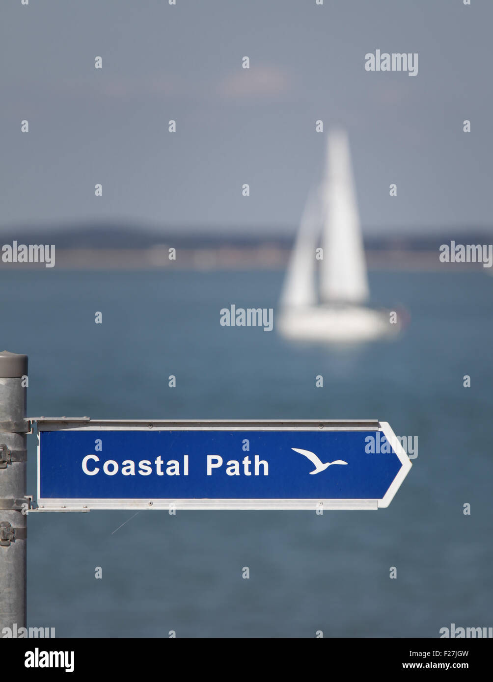 A coastal path sign with a sailing yacht in the background Stock Photo