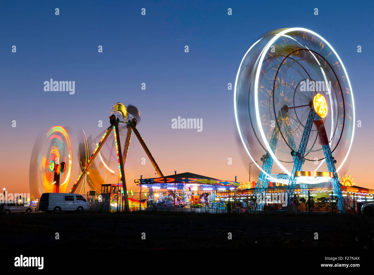Colorful carnival Ferris wheel and gondola spinning in motion blurred at twilight in an amusement park Stock Photo