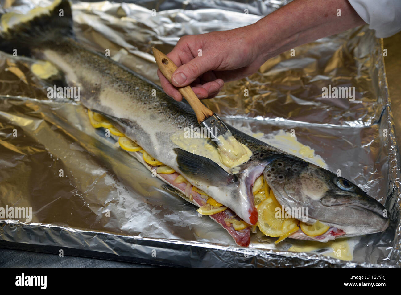 A cook gently bastes a brown trout with butter before it goes in the oven Stock Photo Alamy