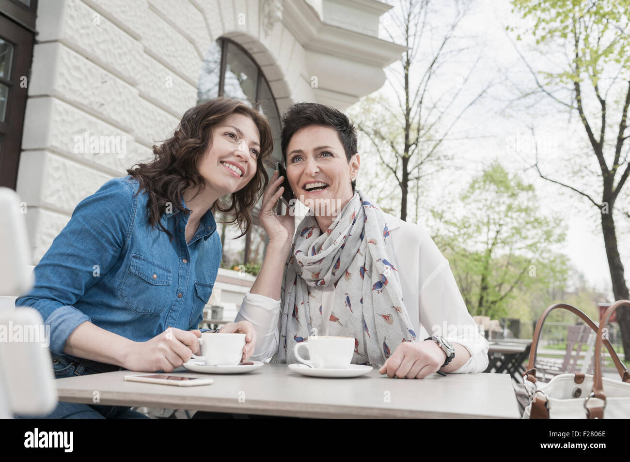 Two friends in the sidewalk cafe and phoning, Bavaria, Germany Stock Photo