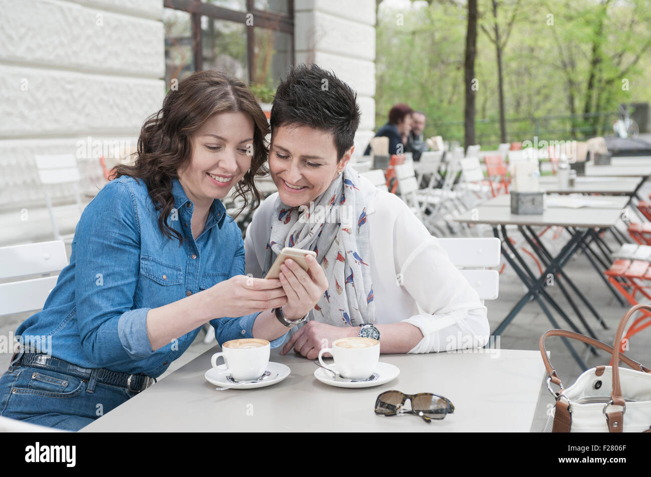 Two friends in the sidewalk cafe looking at phone, Bavaria, Germany Stock Photo
