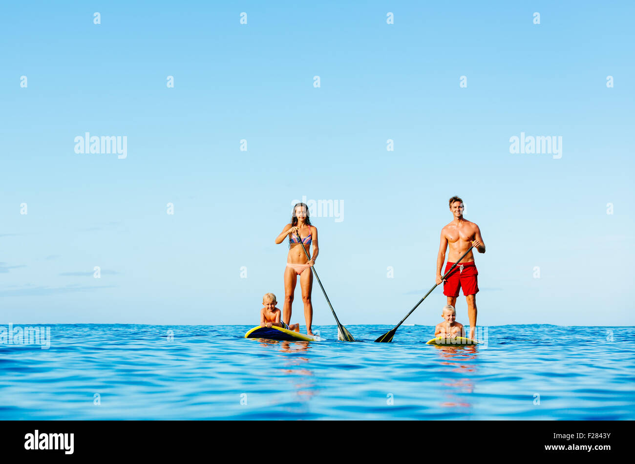 Family Having Fun Stand Up Paddling Together in the Ocean on Beautiful Sunny Morning Stock Photo
