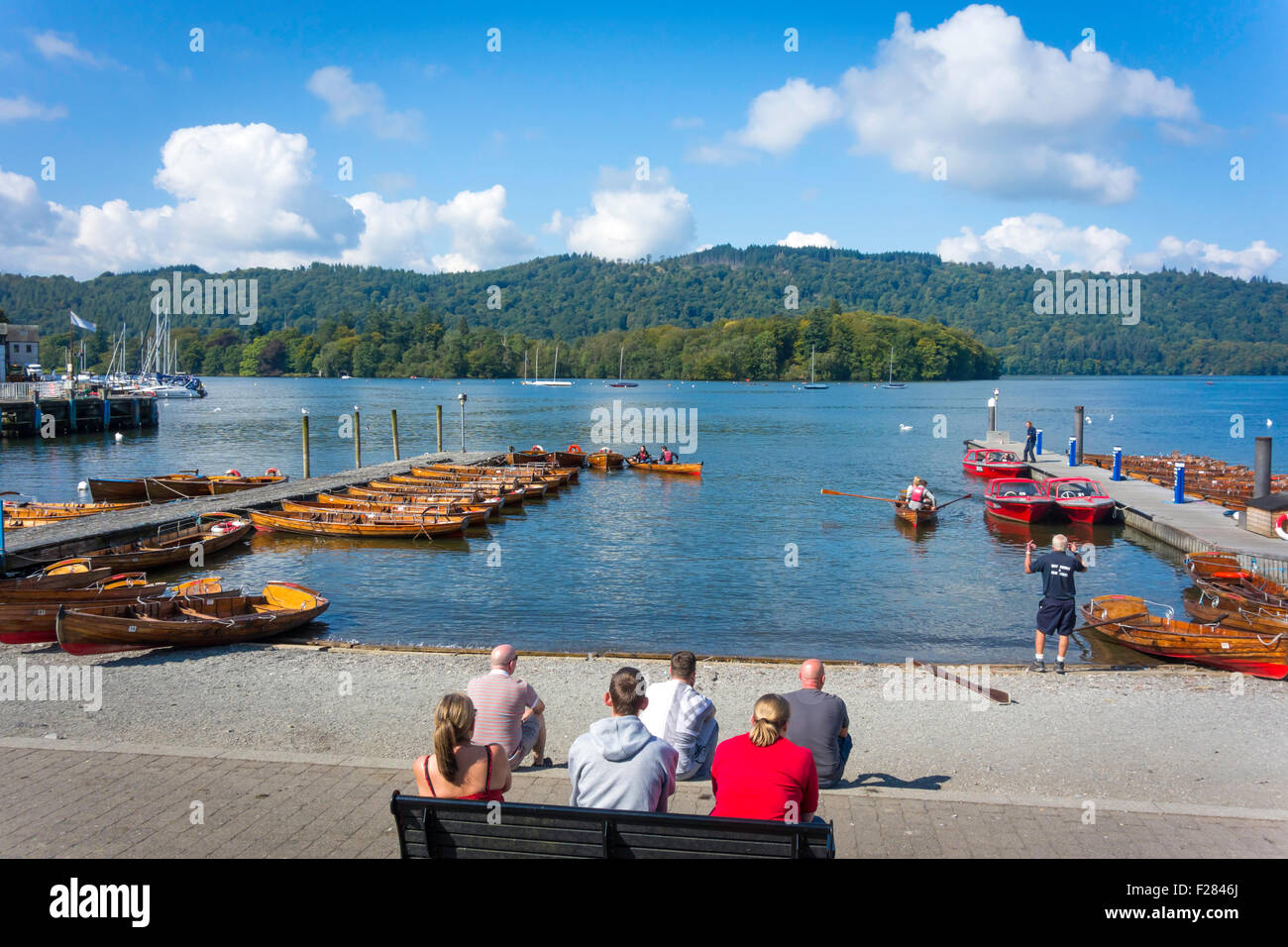 Tourists sitting enjoying autumn sunshine by the piers where traditional wooden skiffs may be hired Bo'ness Windermere Cumbria Stock Photo