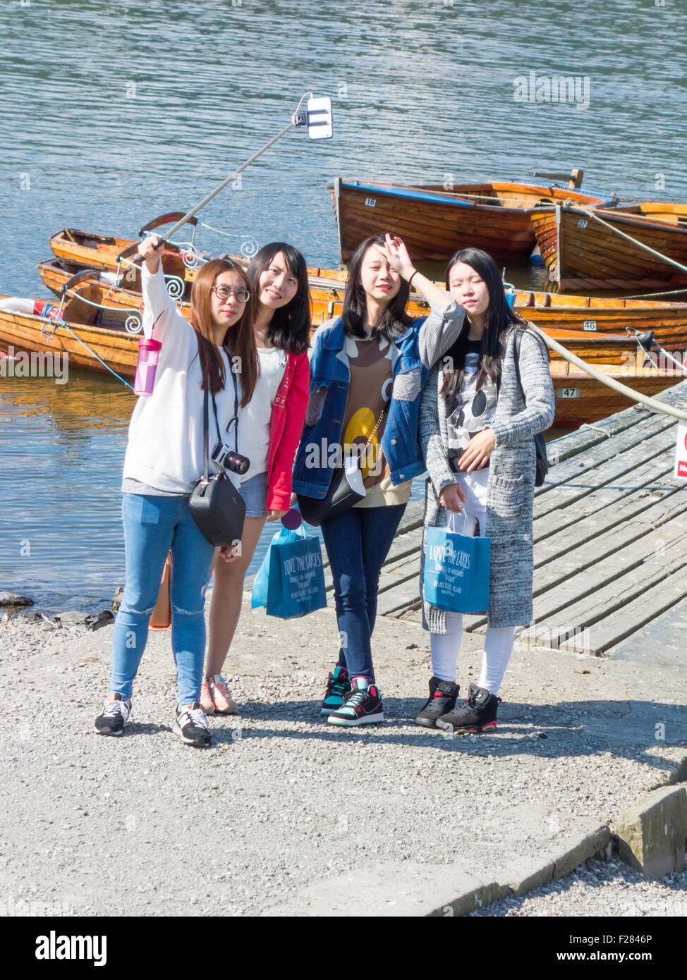 A group of young Asian women using a selfie stick to photograph themselves at Lake Windermere Cumbria Stock Photo