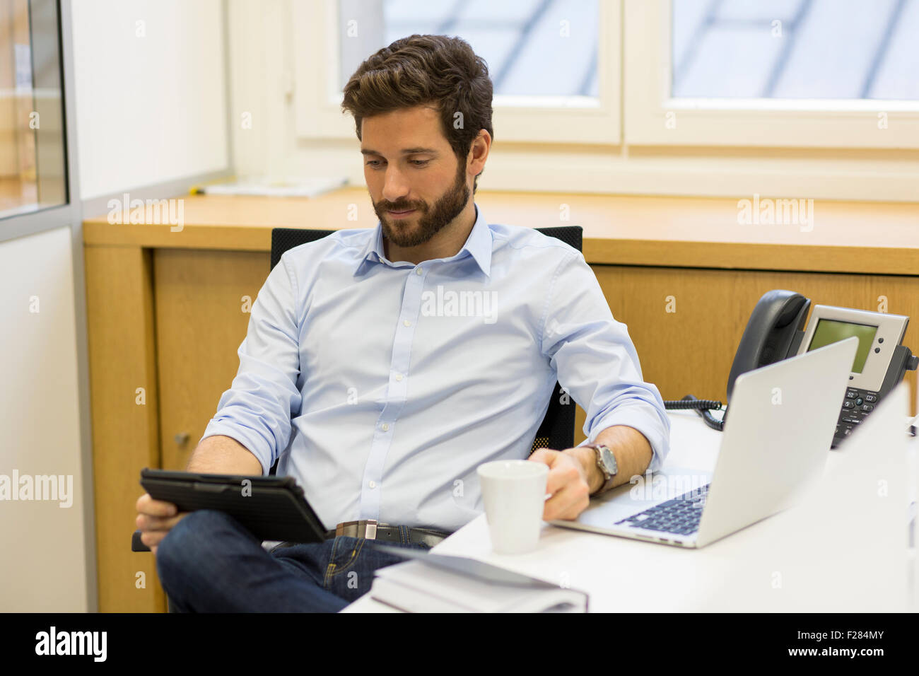 Portrait of businessman holding coffee cup and using digital tablet in office Stock Photo