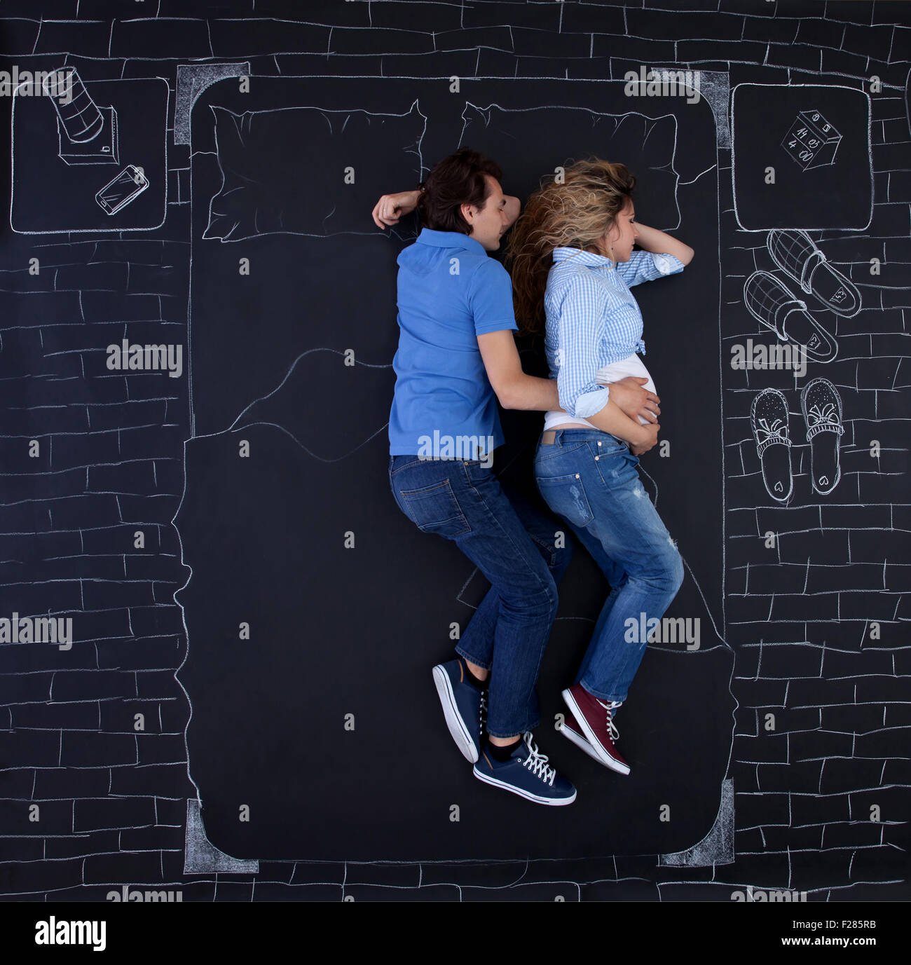 Young couple sleeping in bed, holding hands, the man is embracing his woman. Young dad sleeping with a hand on mom's belly. Stock Photo