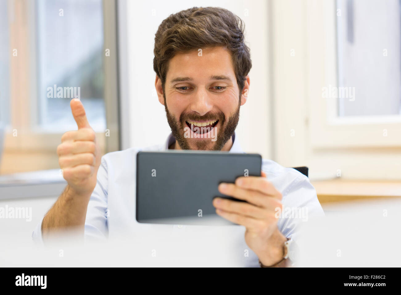 Cheering businessman with thumb up in office using digital tablet Stock Photo