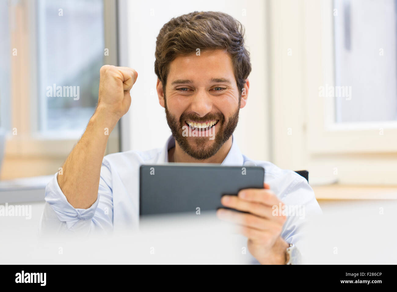 Cheering businessman with punch up in office using digital tablet Stock Photo