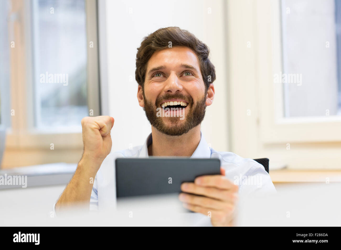 Cheering businessman with punch up in office using digital tablet Stock Photo