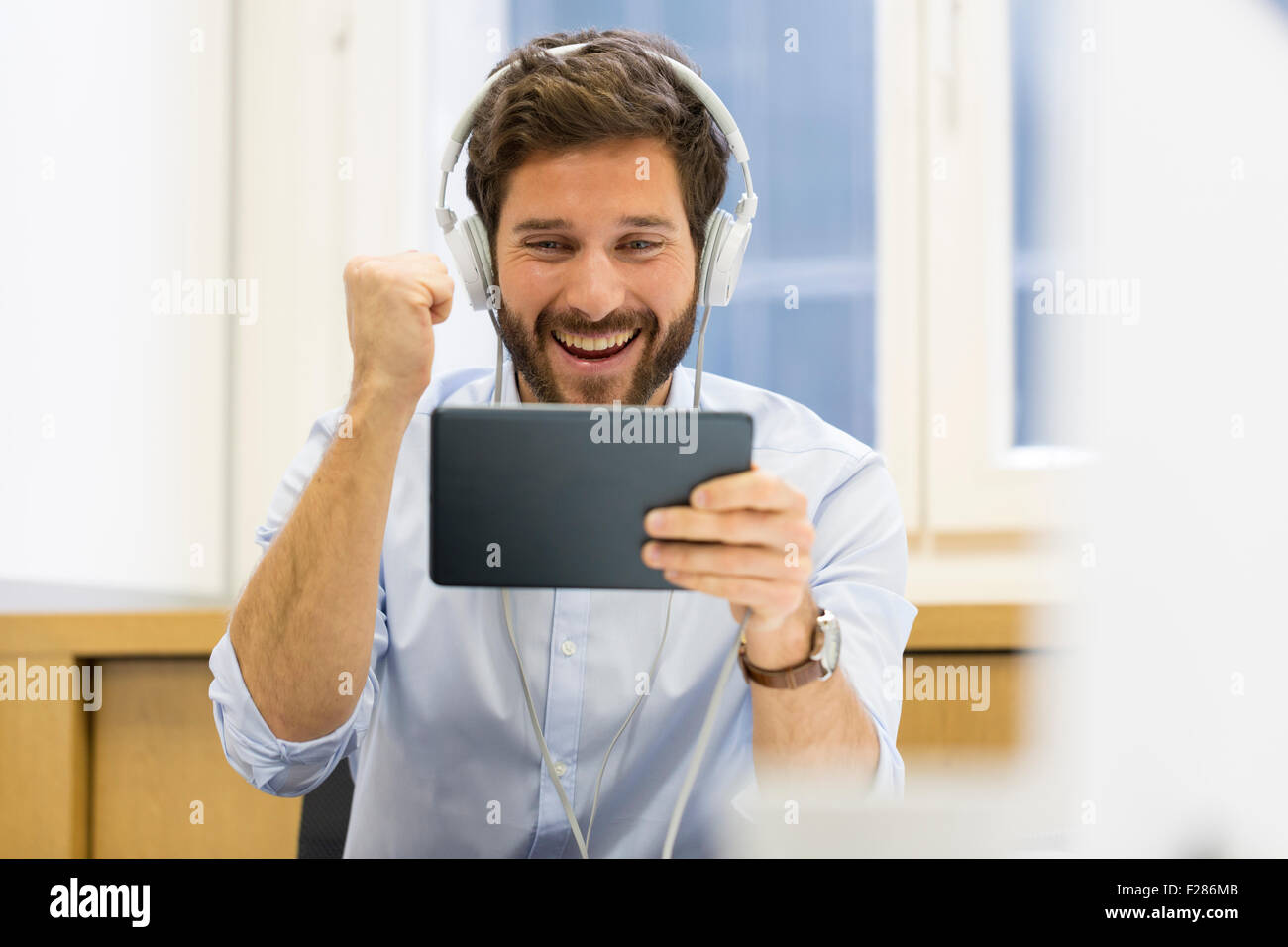 Creative businessman listening to headphones and using digital tablet with punch up in office Stock Photo