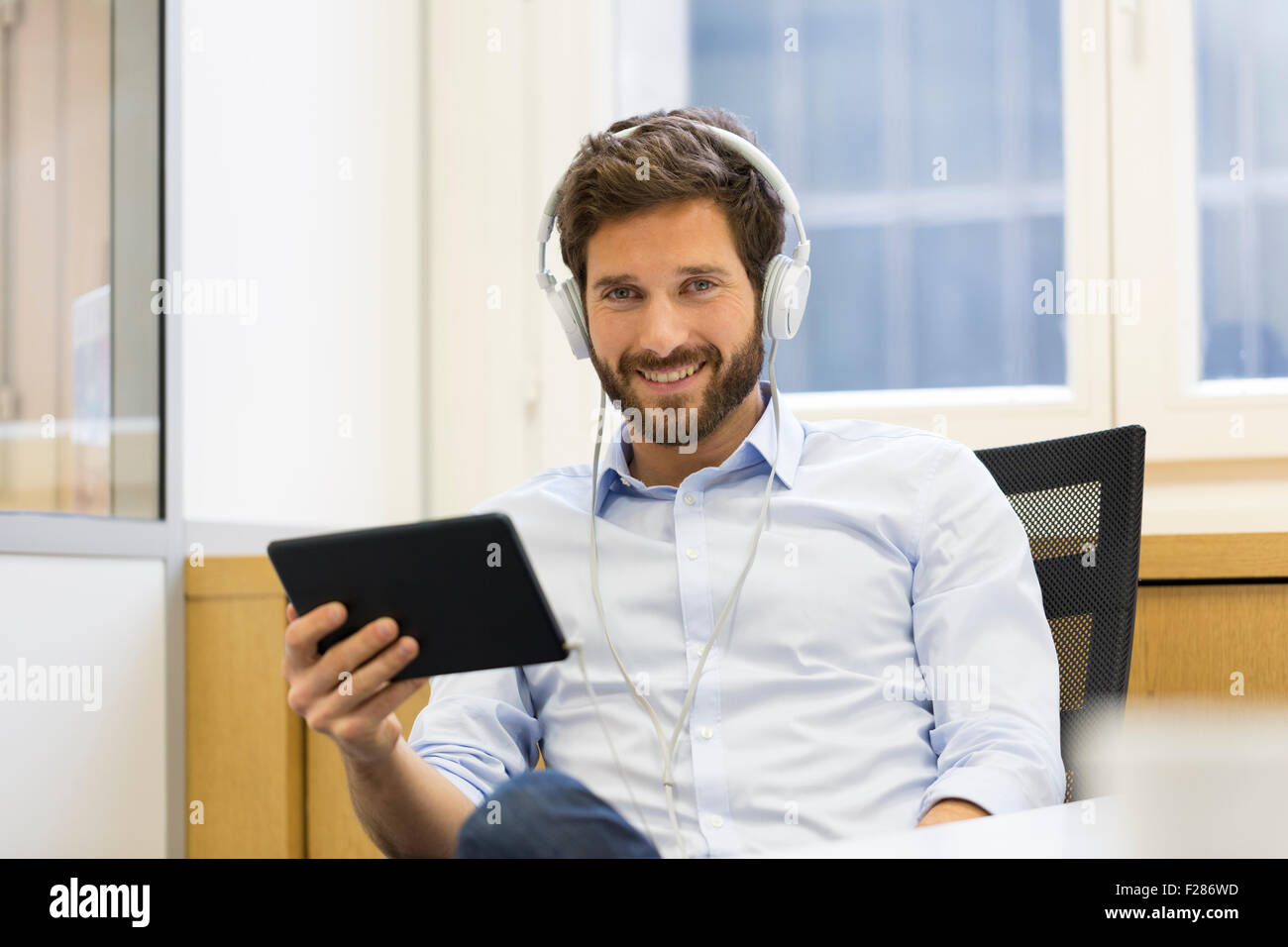 Cheering creative businessman listening to headphones and using digital tablet. Stock Photo