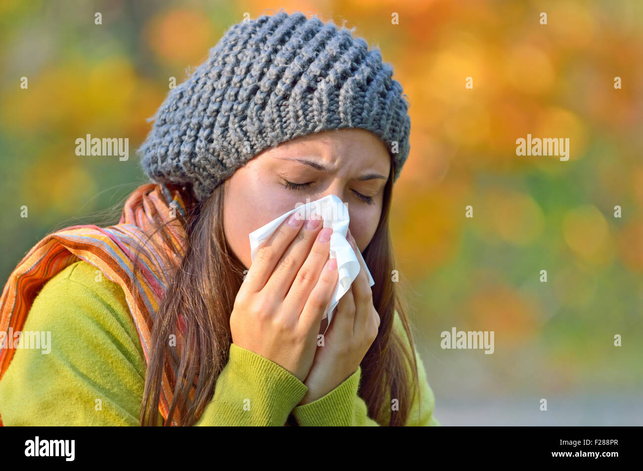 Girl in fall autumn park sneezing in tissue. Stock Photo